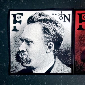 May include: Two black and white stickers with a portrait of a man with a mustache and the text "F...N" in a stylized font. The sticker on the left is white with black text and the sticker on the right is red with white text.
