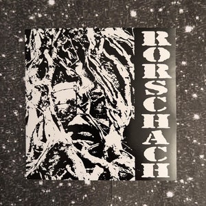 May include: Black and white image of a face obscured by branches, with the word "RORSCHACH" printed vertically on the right side.