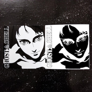 Peut inclure: Deux impressions d'art carrées présentant une illustration en noir et blanc d'un visage de femme. Le texte "GHOST IN THE SHELL" est imprimé verticalement sur le côté gauche de chaque impression. Une impression est positive, l'autre est négative.