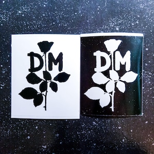 May include: Two black and white stickers with a rose and the letters "DM" in the center. The rose is stylized with a single stem and leaves.