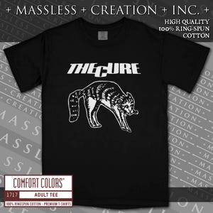 May include: Black adult tee featuring the band name "THE CURE" in white block letters above a black and white raccoon graphic. The shirt is made of 100% ring-spun cotton. The Comfort Colors brand logo is at the bottom.