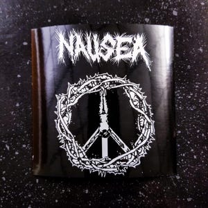 Könnte beinhalten: Schwarz-weißer Aufkleber mit dem Wort "NAUSEA" in Heavy-Metal-Schrift und einem Peace-Zeichen, das von Dornen umgeben ist.
