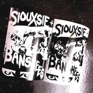 May include: Black and white promotional flyers for Siouxsie and the Banshees. The flyers feature the band's name in bold, white lettering and a black and white image of the band.