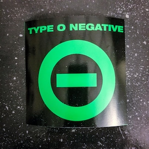 May include: A black and green sticker with the text "TYPE O NEGATIVE" and a green circle with a black horizontal line through it.