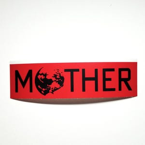 May include: A red sticker with the word "MOTHER" in bold black letters. The letter "O" is replaced with a black graphic of a planet. The sticker has a white border and is set against a white background.