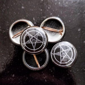 May include: Five black and white button badges featuring a pentagram with a goat's head inside. The badges are displayed on a black surface.