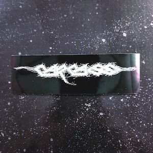 Op de afbeelding: Zwart-witte sticker met het woord "CARCASS" geschreven in een gestileerd, gekarteld lettertype.