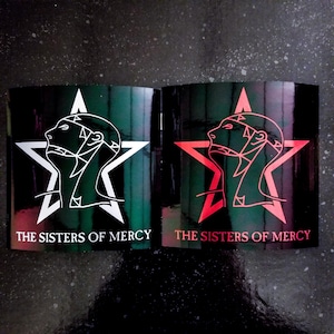 Op de afbeelding: Twee zwarte en groene stickers met een witte ster en een gestileerd hoofd erin. De tekst "THE SISTERS OF MERCY" is in wit gedrukt op de sticker links en in rood op de sticker rechts.