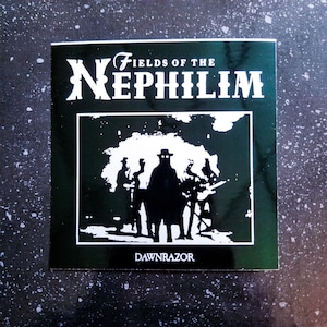 Könnte beinhalten: Quadratischer Aufkleber mit dem weißen Text "FIELDS OF THE NEPHILIM" über einer schwarzen Silhouette einer Figur mit Hut und anderen Figuren. Das Wort "DAWNRAZOR" steht darunter.