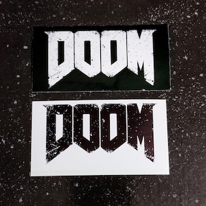 Peut inclure: Deux autocollants avec le mot "DOOM" en police blanche vieillie sur fond noir et en police noire sur fond blanc.
