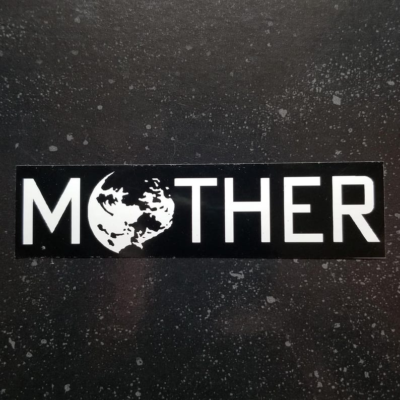 May include: A black rectangular sticker with the word "MOTHER" in bold white capital letters. The "O" is replaced by a white graphic of a planet with a crescent moon shape. The background is a dark, speckled surface.