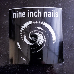 May include: Black and white sticker with the text "nine inch nails" and a spiral design.