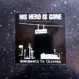 Puede incluir: Pegatina en blanco y negro con el texto "HIS HERO IS GONE" y "monuments to thieves". La pegatina también presenta un gráfico de un edificio con un letrero que dice "Auction".