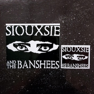 May include: Two black and white stickers with the text "Siouxsie and the Banshees" and a stylized image of eyes.