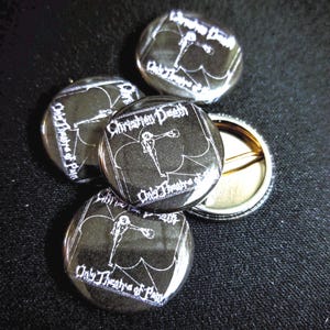 May include: Four silver metal button pins with a black and white image of a skeleton holding a microphone. The text on the pins reads "Christian Death" and "Only Theatre of Pain".