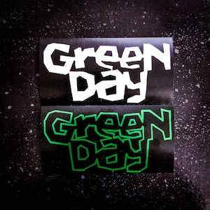 May include: Two black and white stickers with the text "Green Day" in a bold, stylized font. The top sticker has white text on a black background. The bottom sticker has green text on a black background.