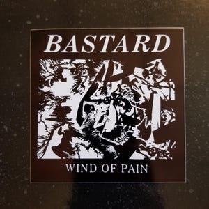 Könnte beinhalten: Schwarz-weißer Aufkleber mit dem Bandnamen "BASTARD" und dem Albumtitel "WIND OF PAIN". Der Aufkleber zeigt ein chaotisches, abstraktes Design.