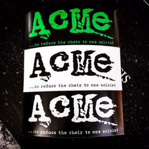 May include: Three black and white stickers with the word "ACME" in a bold, stylized font. The text "...to reduce the choir to one soloist" appears below each sticker.