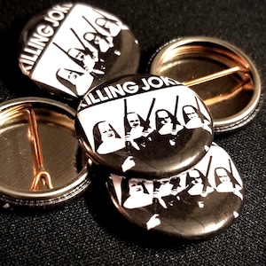 Puede incluir: Cuatro pines de botón negros y blancos con el texto "Killing Joke" y una banda de figuras con túnicas negras.