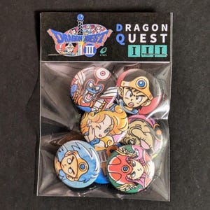 May include: A set of eight Dragon Quest III pins featuring various characters from the game. The pins are round and have a glossy finish. The characters are depicted in a cartoon style and are colorful. The pins are packaged in a clear plastic bag with a header card that reads "Dragon Quest III".