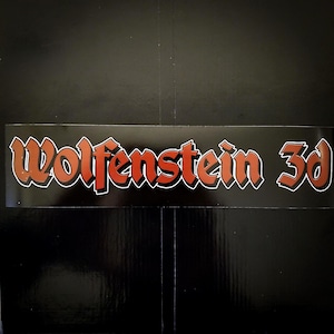 May include: A rectangular sticker with the text "Wolfenstein 3d" in a stylized, orange and red font with a white outline. The sticker is on a black background.