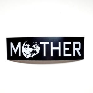 May include: A black rectangular sticker with the word "MOTHER" in bold white capital letters. The letter "O" is replaced with a white graphic of a celestial body, possibly a moon or planet.