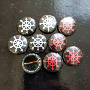 May include: Eight black and white button badges with a red and white symbol. The symbol is a circle with eight spokes and arrows pointing outwards. The badges are arranged in a circle around a single badge with a blank back.