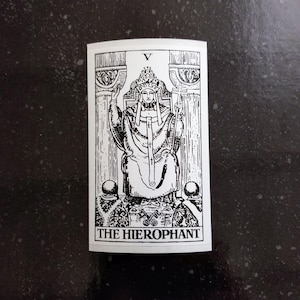 May include: Black and white illustration of The Hierophant tarot card. The card depicts a figure wearing a crown and robes, seated on a throne with two pillars behind them. The card number, V, is displayed in the top right corner.