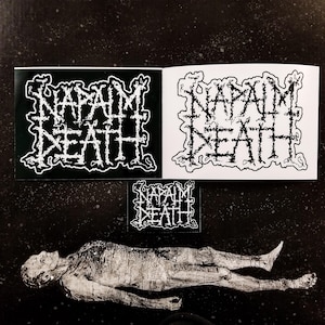 May include: A black and white image featuring three stickers with the band name "NAPALM DEATH" in a stylized, jagged font. The stickers are on a dark, speckled background, with a grayscale illustration of a human figure at the bottom.
