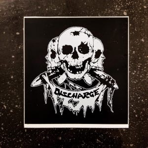 May include: Black and white sticker with a skull graphic and the word "DISCHARGE" in a banner.