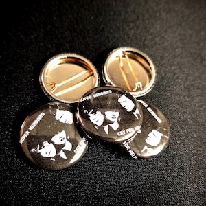 May include: Four black and white button pins with the text "Super Heroines" and "Cry For Help". The pins feature a black and white image of three women with short hair.