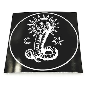 May include: Black and white sticker with a circular design featuring a coiled snake with a sun, moon, and star above it.