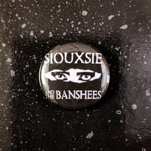 Op de afbeelding: Een zwart-witte knop met de tekst "Siouxsie and the Banshees" en een paar ogen.