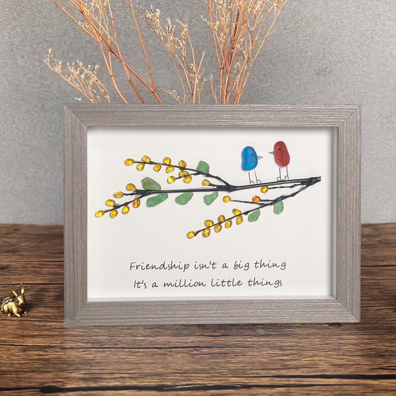 May include: Framed artwork featuring a branch with yellow and green glass beads, two birds made of glass, one blue and one red, perched on the branch. The quote "Friendship isn't a big thing, it's a million little things" is written below the branch.
