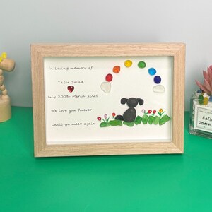 May include: A framed memorial for a dog named Tater Salad. The frame features a rainbow made of colourful glass stones, a black dog made of stones, and a red heart. The text reads "In loving memory of Tater Salad, July 2003- March 2025, We love you forever, Until we meet again."