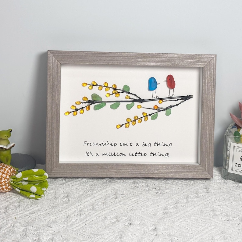 May include: A framed artwork featuring a branch with yellow and green glass beads, two birds made of blue and red glass, and the quote "Friendship isn't a big thing, it's a million little things".