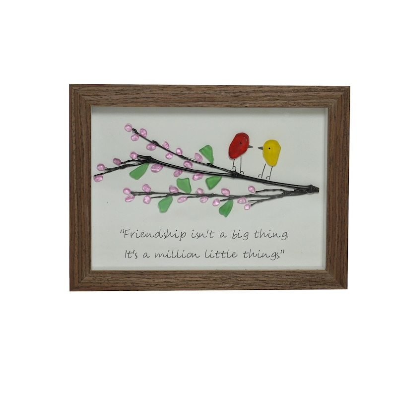 May include: Framed artwork featuring two glass birds perched on a branch with pink and green glass flowers. The quote "Friendship isn't a big thing. It's a million little things." is written below the birds.