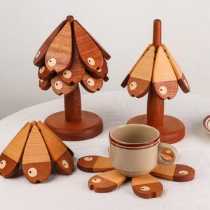 Puede incluir: Posavasos y soportes decorativos de madera con forma de pez. Los posavasos rodean una taza beige con rayas marrones. Los soportes tienen un diseño de árbol con elementos en forma de pez.