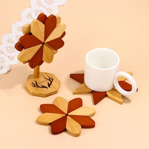 May include: Wooden flower-shaped coasters and a matching decorative piece. The coasters and decorative piece are made of alternating light and dark brown wood. A white mug sits on one coaster. The decorative piece has a wooden base with the name "Melissa" and deer antlers.