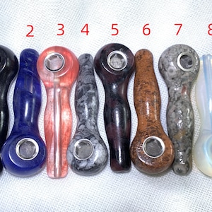 Op de afbeelding: Acht handgesneden stenen pijpen, elk met een uniek ontwerp en kleur. De pijpen zijn genummerd van 1 tot 8.