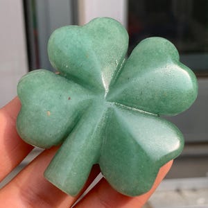 Può includere: Un quadrifoglio verde scolpito in una pietra liscia e lucida. Il quadrifoglio è un simbolo popolare di buona fortuna e fortuna.