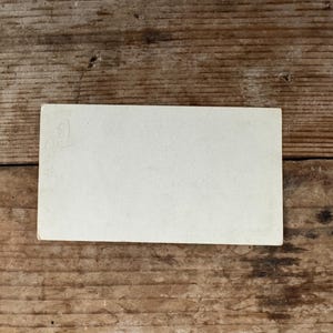 Puede incluir: Una tarjeta blanca en blanco con una tenue marca de l&aacute;piz en la esquina superior izquierda. La tarjeta est&aacute; sobre una superficie de madera.