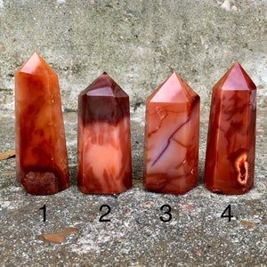 May include: Four carnelian crystal points, each with a unique pattern of red, orange, and white banding. The points are arranged in a row from left to right, numbered 1 through 4.