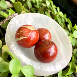 Può includere: Tre sfere di diaspro rosso con venature bianche, appoggiate su un piatto di selenite bianca. Le sfere sono lisce e lucidate.