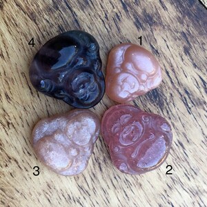 May include: Four small glass figurines of the Japanese deity Hotei, also known as the "Laughing Buddha". The figurines are in various shades of pink and purple.