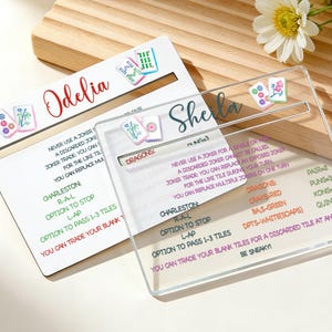 May include: Two personalized Mahjong scoreboards. One is white with the name "Odelia" in red script, the other is clear with the name "Sheila" in blue script. Both have Mahjong tile graphics and game instructions.