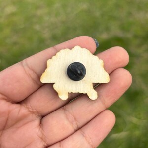 May include: Wooden pin of a cartoon hedgehog with a black pin back.