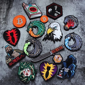 May include: A collection of embroidered patches featuring diverse designs including a cigarette pack labelled First Strike Death Sticks, a Bitcoin logo, a dragon, a bald eagle, a bear, a knife, a bee, Medusa, a grim reaper, and heart-shaped icons.
