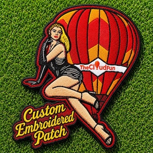 Peut inclure: Un écusson brodé représentant une montgolfière rouge et orange avec le texte TheCloudFun. Une silhouette aux cheveux blonds en robe noire et gants est assise devant le ballon. Le texte Custom Embroidered Patch figure en bas.