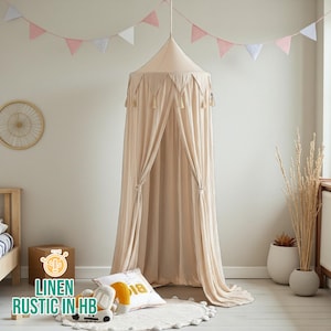 Puede incluir: Un dosel de lino beige con borlas cuelga del techo. El dosel está drapeado, creando un efecto suave y fluido. Una guirnalda de banderas triangulares rosas y blancas decora la habitación. El texto "LINEN RUSTIC IN HB" es visible en una caja.